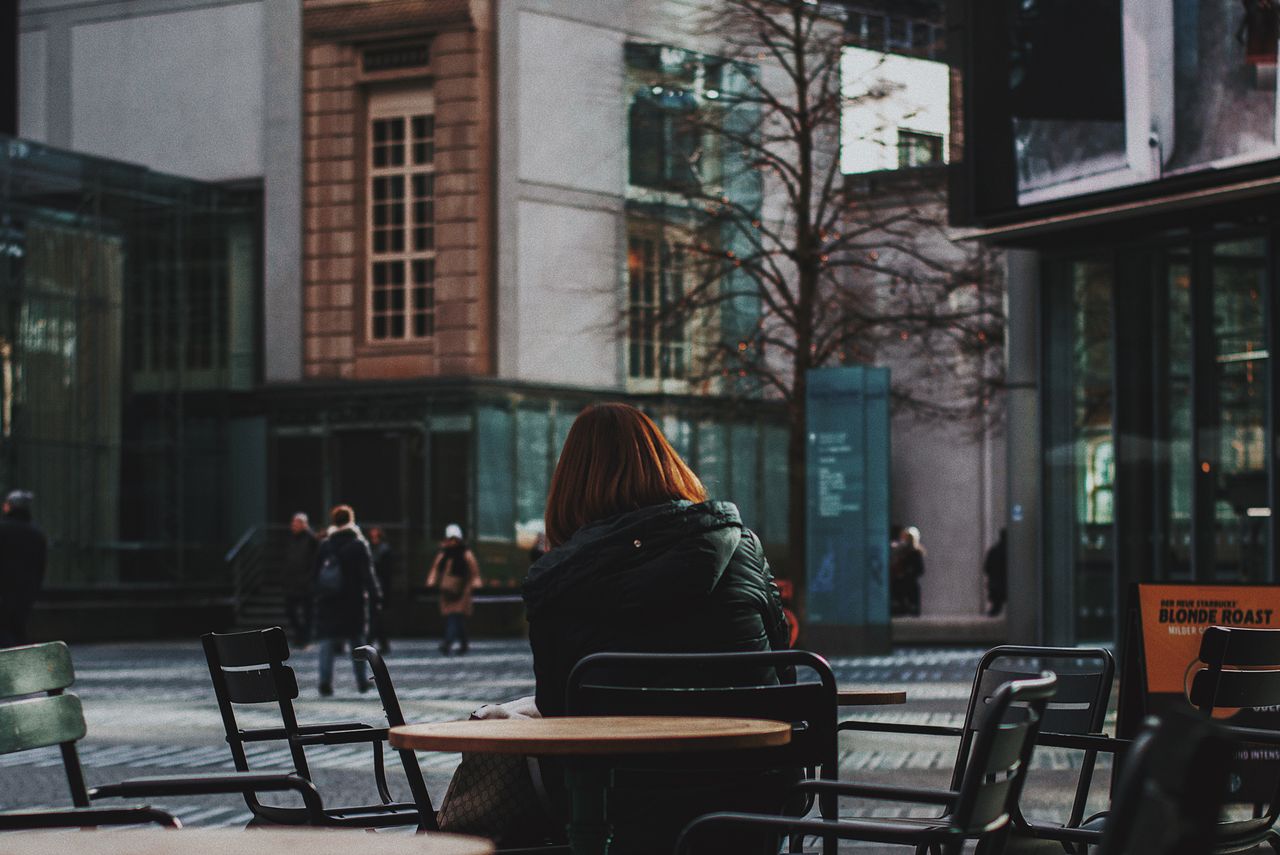 a woman sitting alone at an outdoor cafe surrounded by urban architect