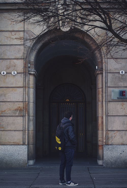 Man Wearing Black Jacket Standing in Front of Building