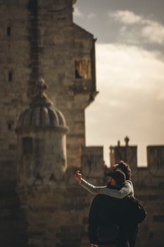 A couple captures a selfie moment in front of a historic stone castle, showcasing romance and travel.