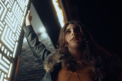 Free A fashionable woman in a black jacket poses confidently against a modern lit structure at night. Stock Photo