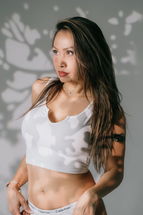 Free Portrait of a woman with long hair in a white top, with artistic shadows on a white background. Stock Photo