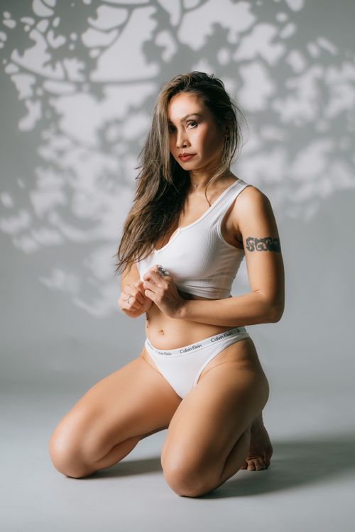 Free Artistic portrait of a woman kneeling in white underwear with long hair on a white background. Stock Photo