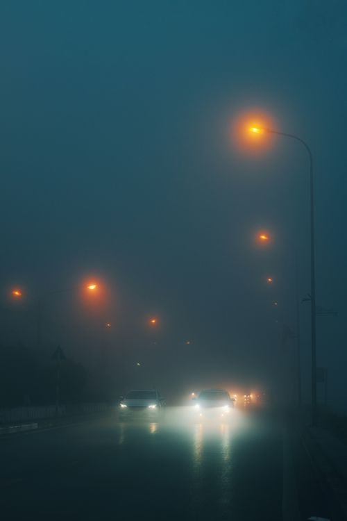 Free A foggy urban street at night with glowing streetlights and car headlights. Stock Photo