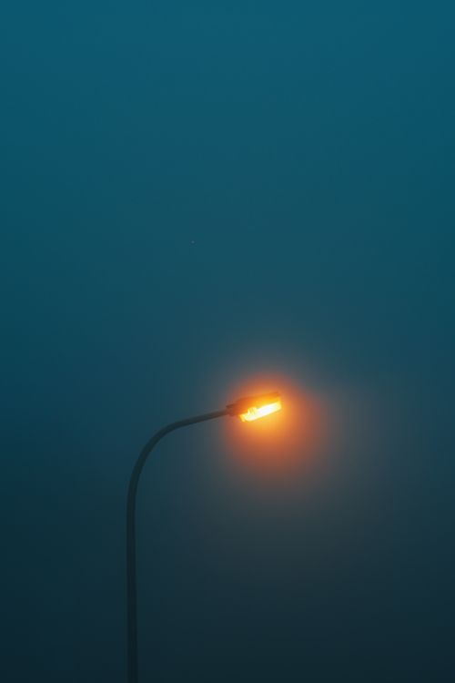 Free A lone street lamp glowing amidst thick fog and darkness, creating a moody atmosphere. Stock Photo