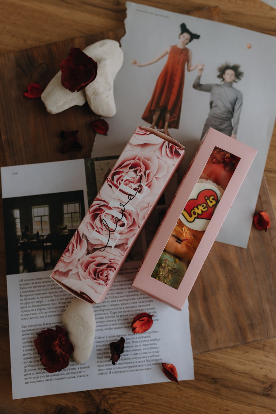 A top view of elegant gift boxes surrounded by rose petals and artistic prints, symbolizing love.