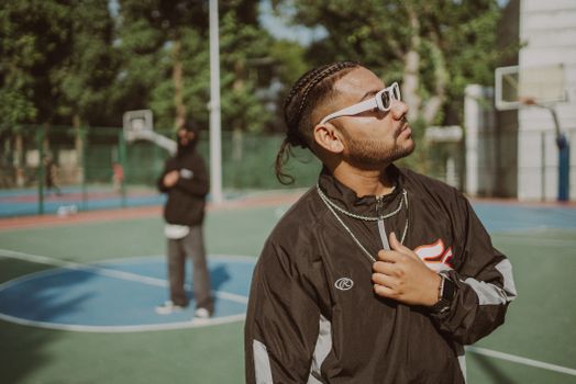 Man in fashionable tracksuit and sunglasses at outdoor basketball court. Urban vibe.