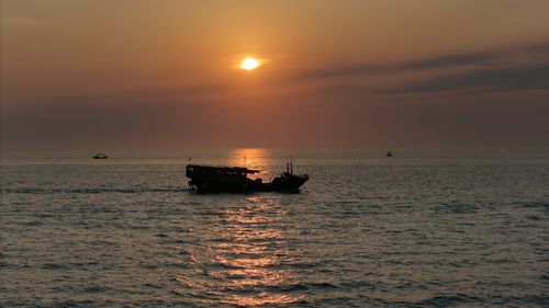 Free A tranquil sunset scene with a silhouetted boat on the calm sea, reflecting warm hues. Stock Photo