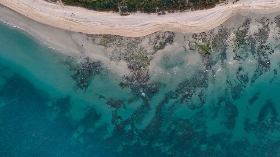 30 minute Reef Scenic Flight - A stunning aerial view of a turquoise beach with rocky shoreline and clear waters.