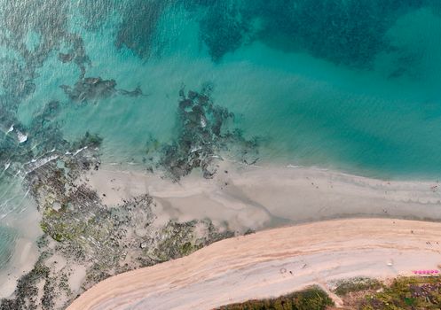 A breathtaking aerial shot capturing a tranquil beach, turquoise ocean, and rocky shoreline, inviting travel and exploration.