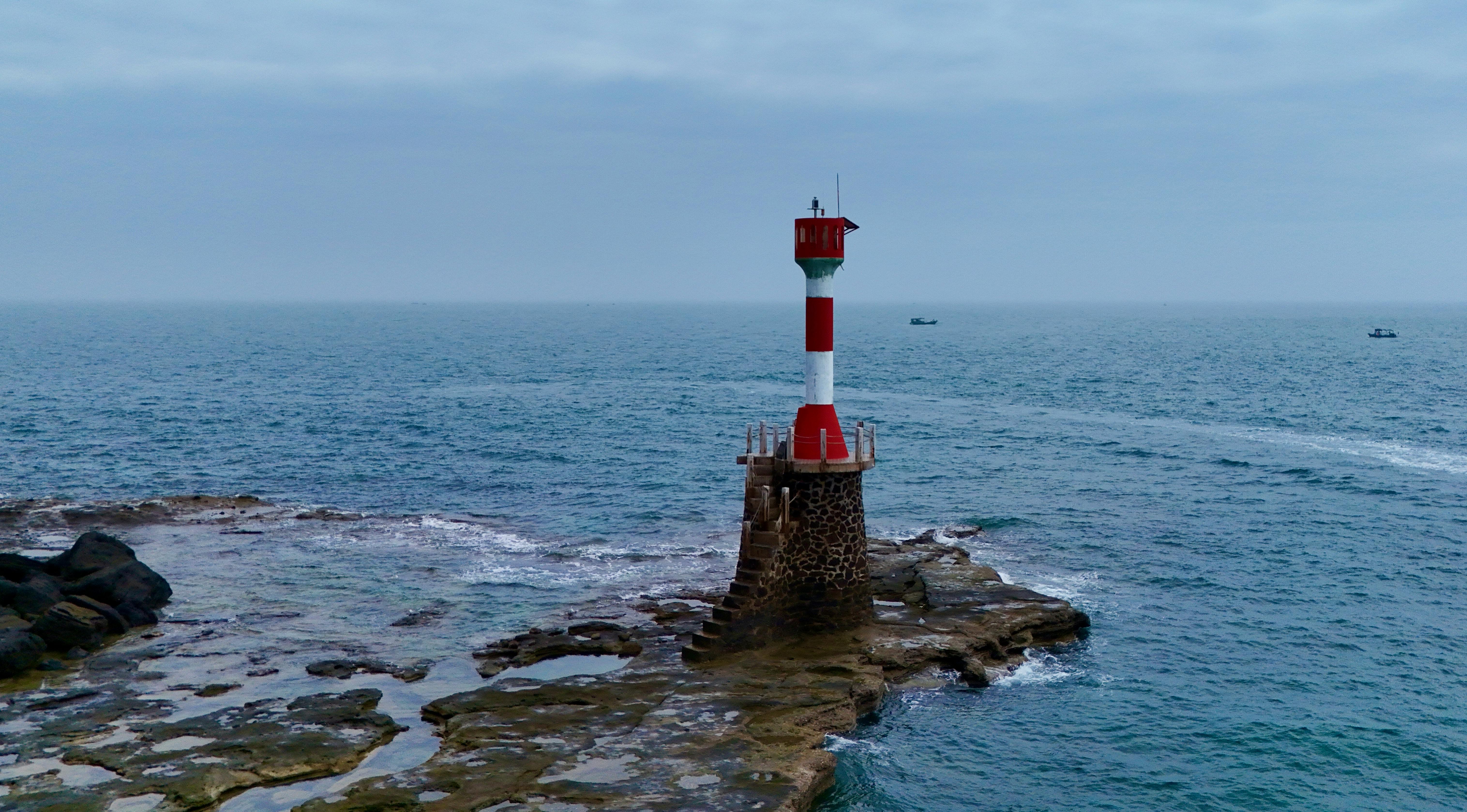 A picturesque red and white lighthouse standing on a rocky coastline overlooking the serene ocean under a cloudy sky.