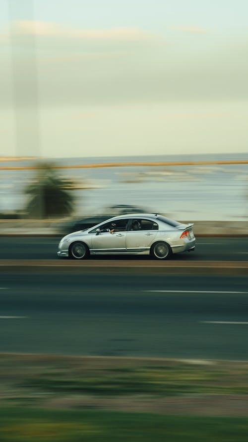 A Silver Honda Car Driving Fast on a Street 