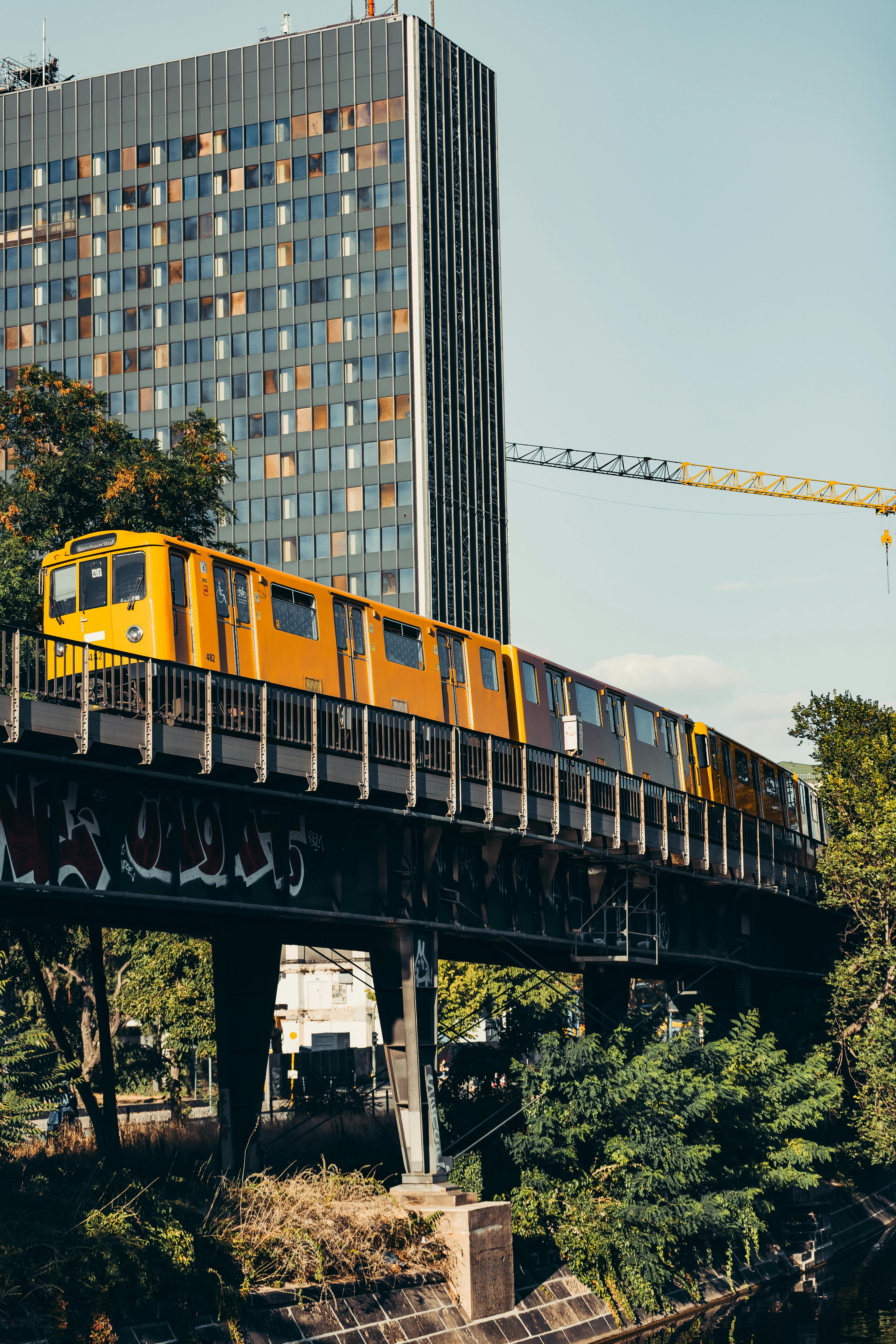 A vibrant yellow train crosses an elevated bridge in Berlin, captured against a backdrop of skyscrapers and clear blue sky.