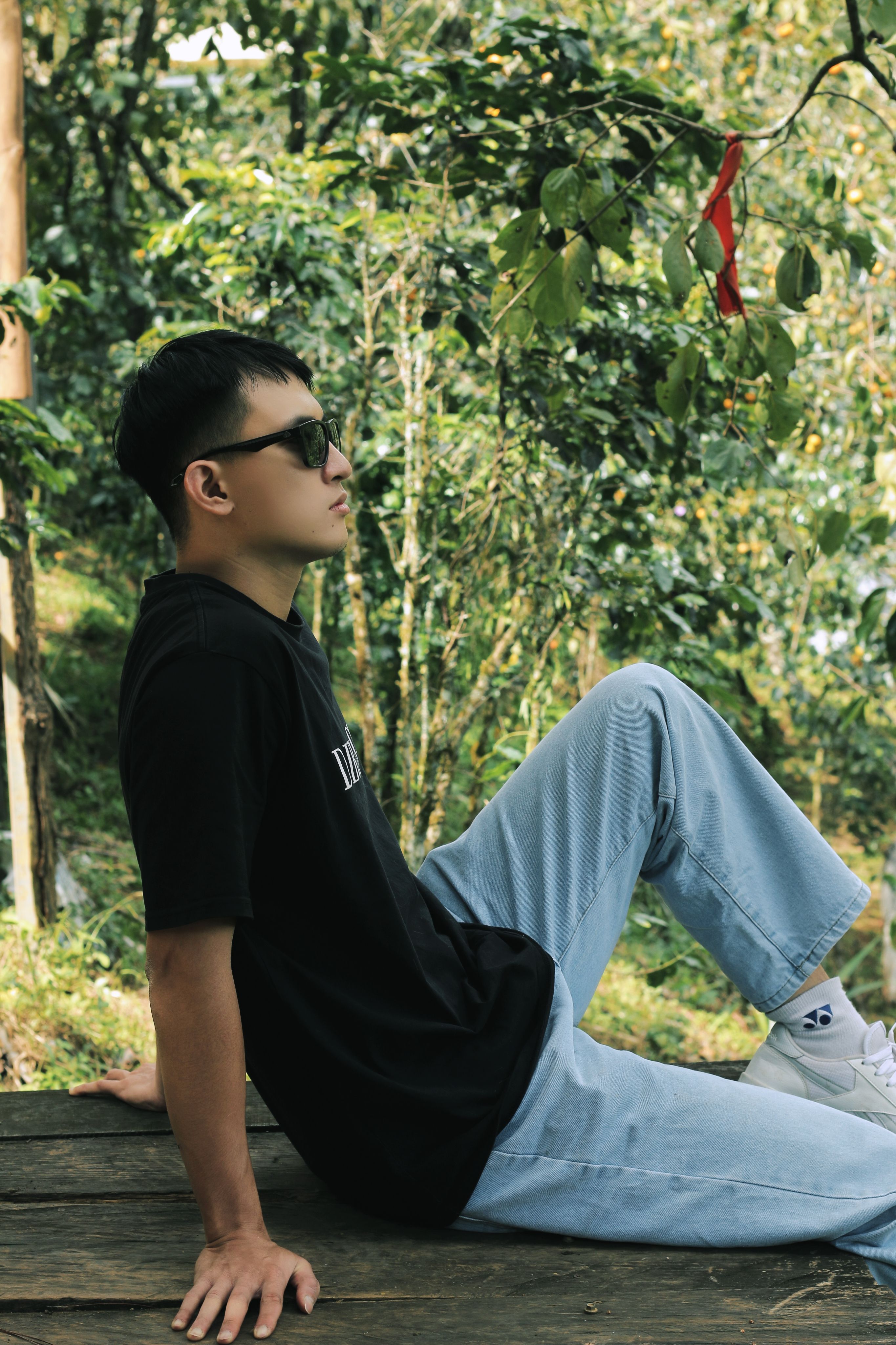 Young man in sunglasses relaxing on a wooden deck in a lush green park.