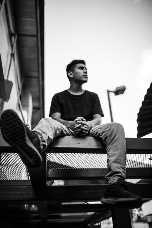 Free A contemplative young man seated on an outdoor structure in black and white. Stock Photo