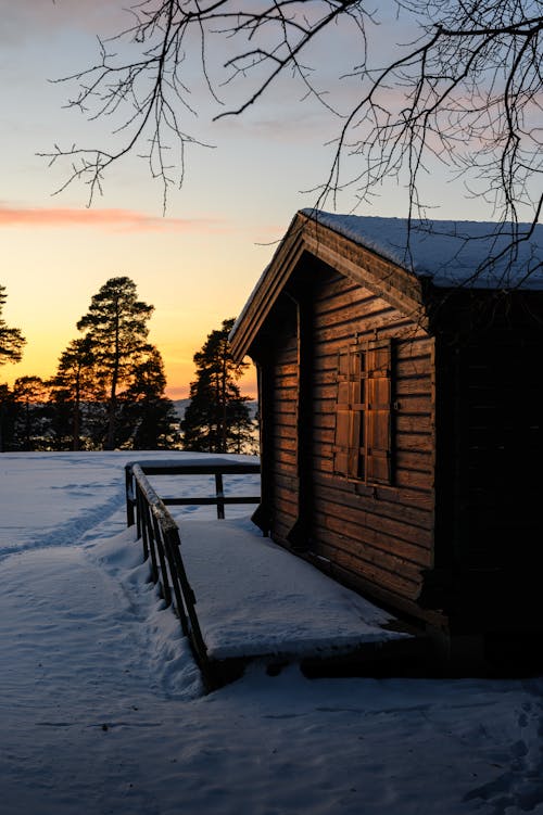 A wooden cabin in the snow at sunset