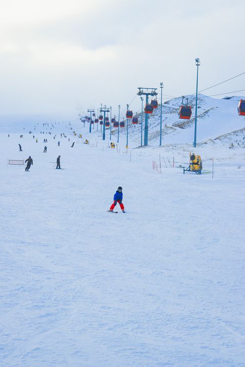 Free Vibrant winter scene of a snowy ski resort with active skiers and cable cars on a bright day. Stock Photo