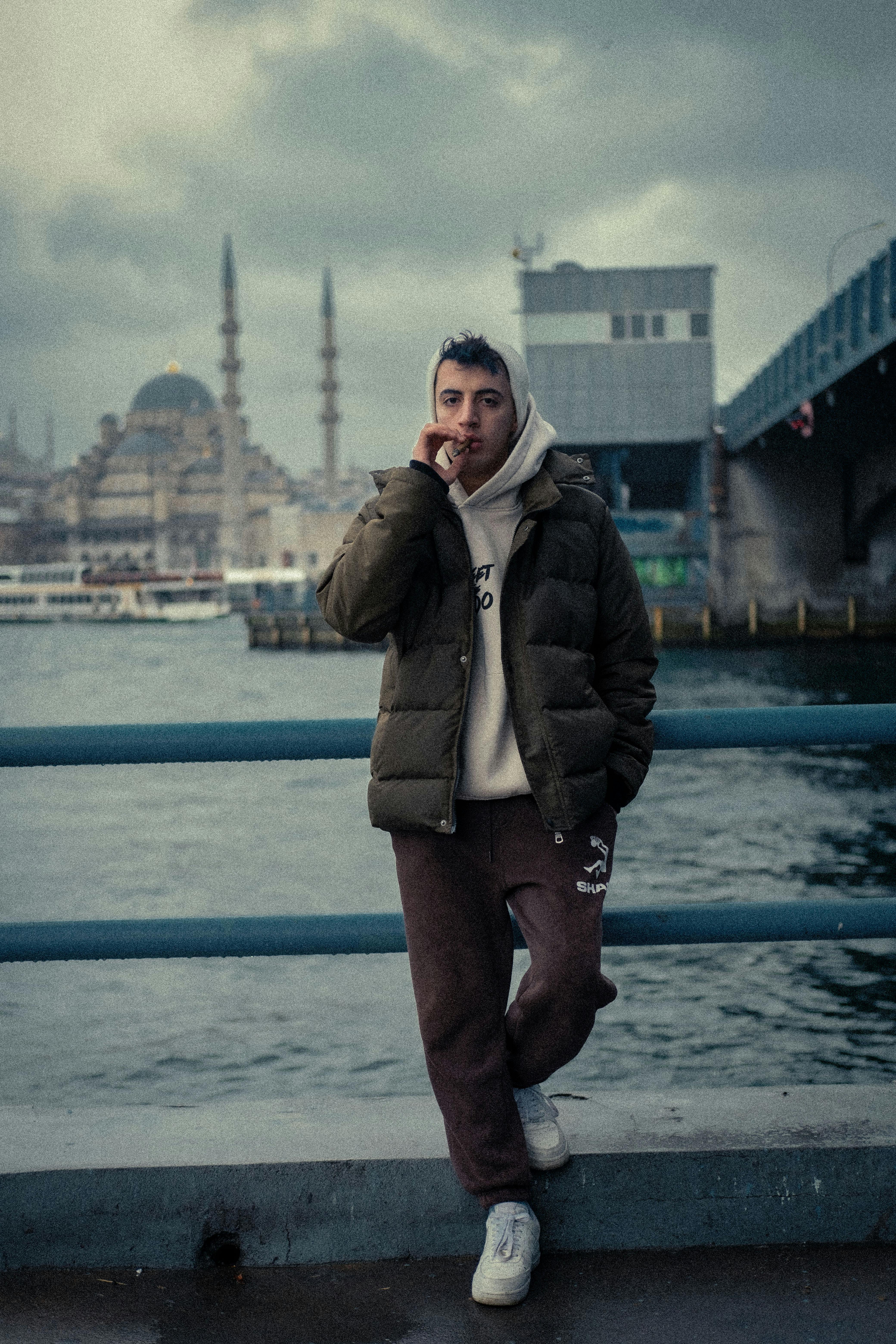 Man standing by the waterfront near Galata Bridge with Istanbul skyline in the background.