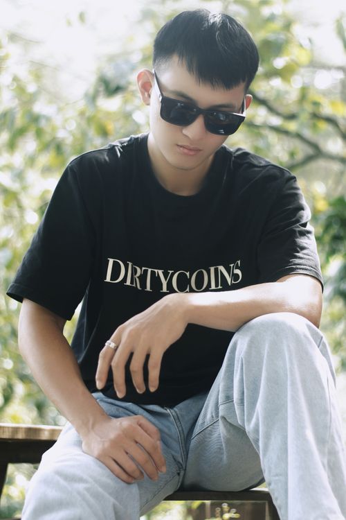 Free Stylish young adult wearing sunglasses, seated outdoors, exuding a cool vibe. Stock Photo