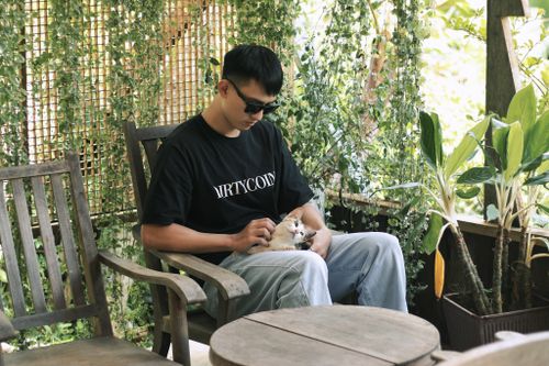 Free Young man relaxing on a patio wearing sunglasses, petting a cat in a tranquil setting. Stock Photo