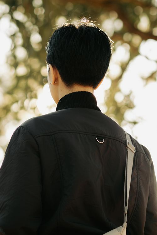 Free A stylish person with short hair wearing a black jacket, captured from behind against a natural background. Stock Photo