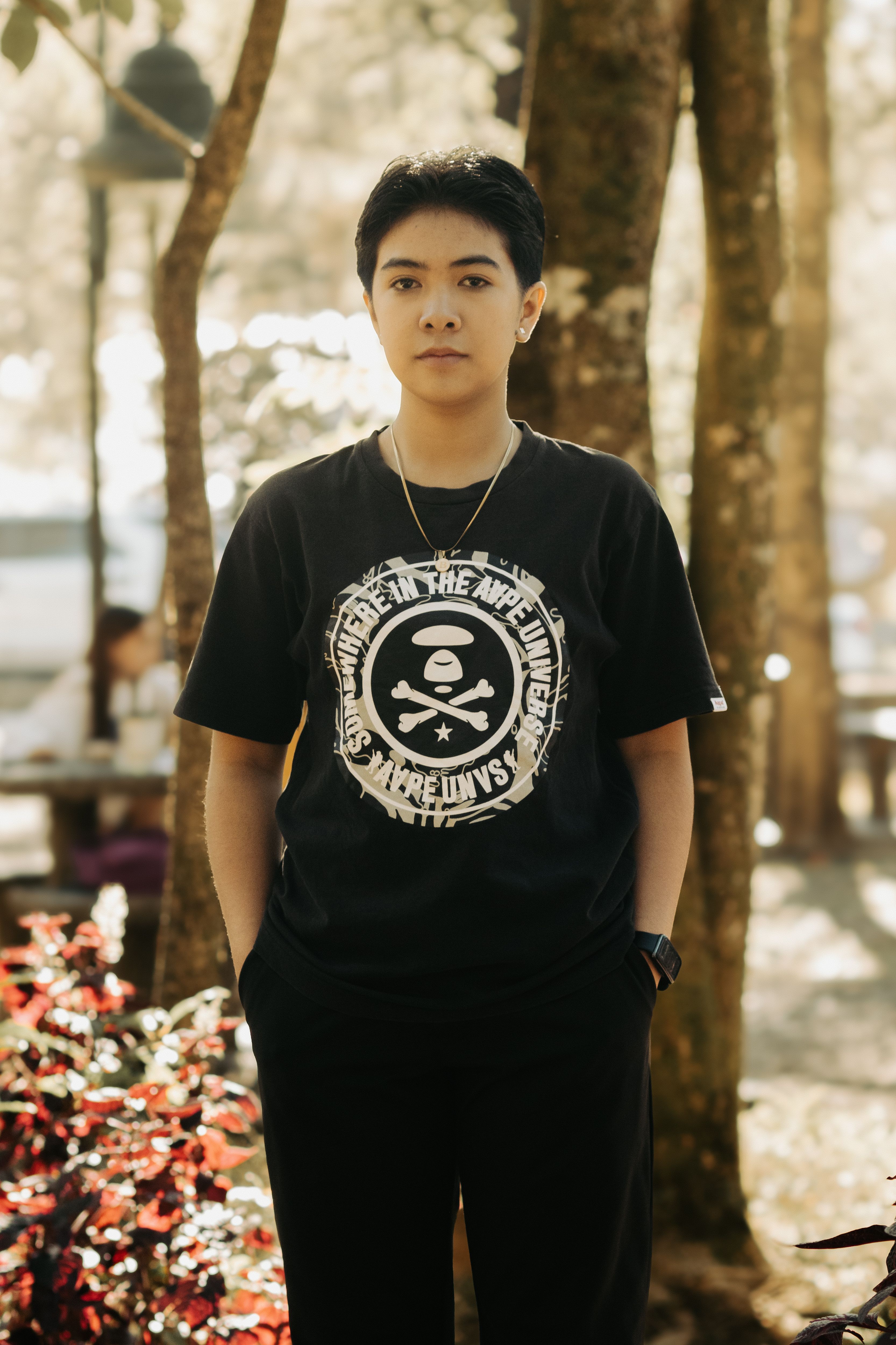 A young adult in a black t-shirt poses confidently in a sunlit forest, embodying casual style.