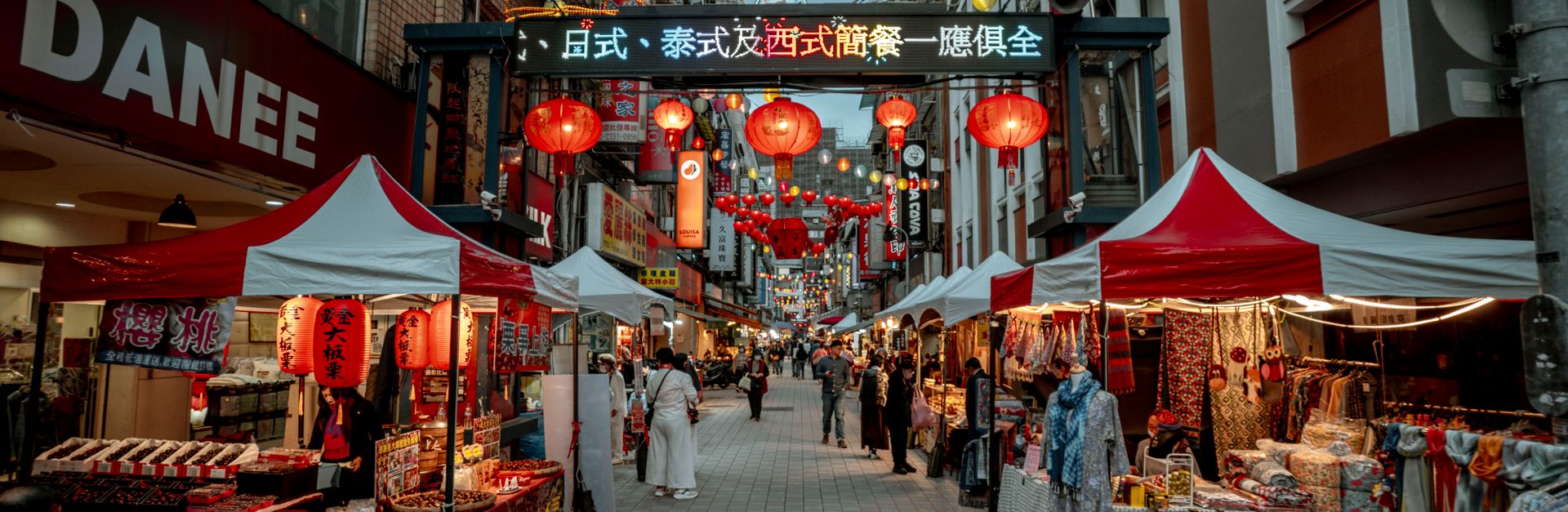 Bustling Asian street market with red lanterns and vibrant stalls offering goods.