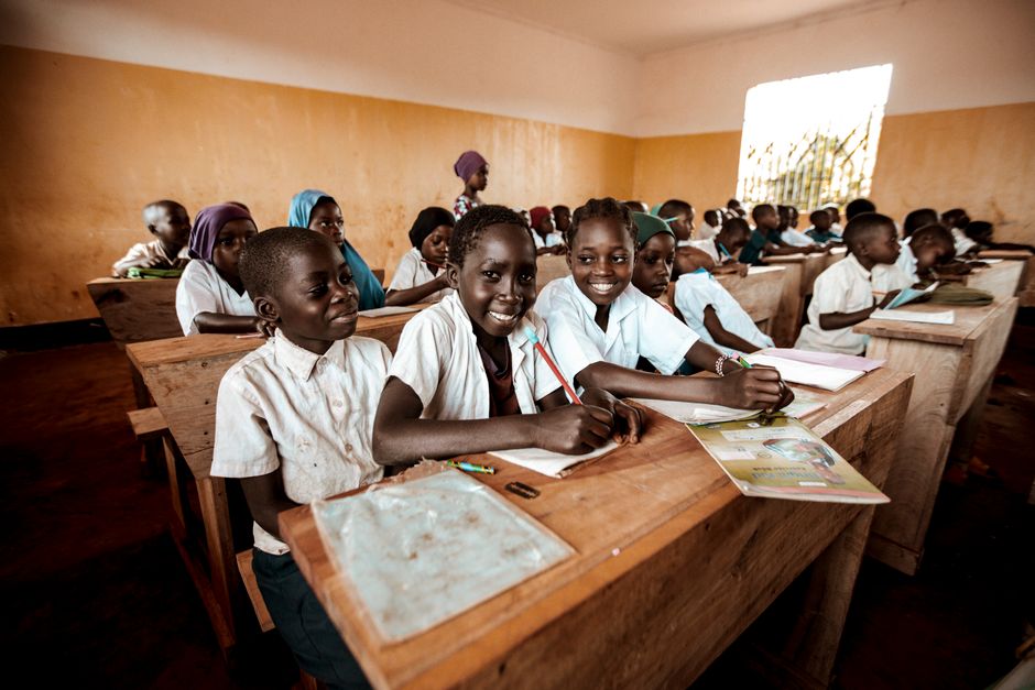 A lively classroom scene with children at wooden desks actively participating in learning.