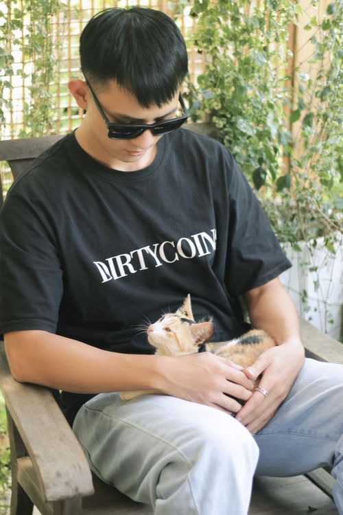 Free A man wearing sunglasses and a black t-shirt sits with a cat in his lap, showcasing a serene outdoor setting. Stock Photo