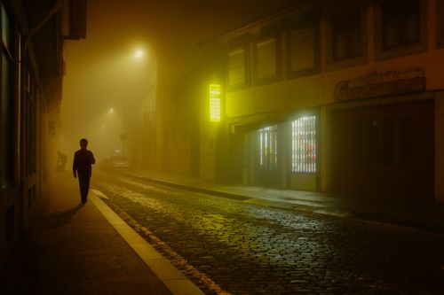 Free A lone figure walks through a foggy, illuminated street in Porto at night. Stock Photo
