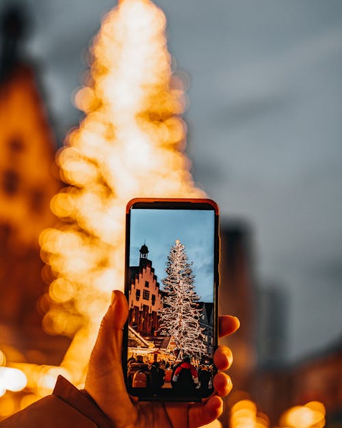 Close-up of a Person Photographing a Christmas Tree with a Smartphone 