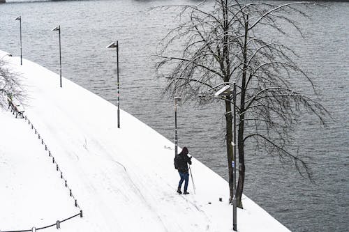 Aerial View of a Man Standing near a River on a Snowy Sidewalk 