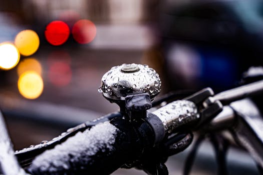 Raindrops on a bicycle bell with blurred city lights in the background, creating a moody urban atmosphere.