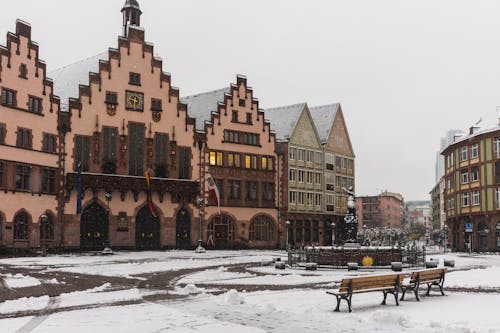 A city square with benches and buildings in the snow