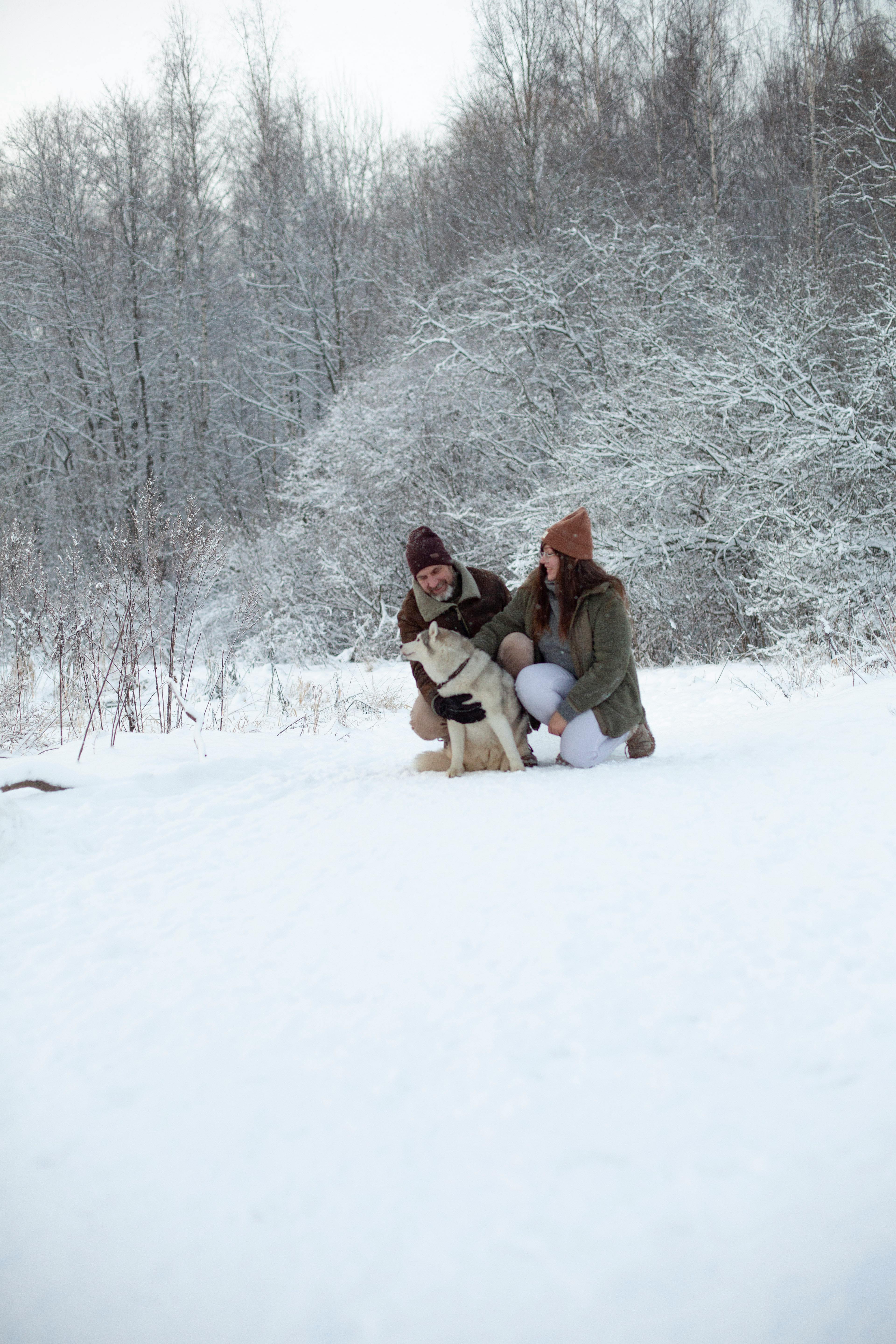 A joyful couple playing with their dog in a snowy forest during a winter day.