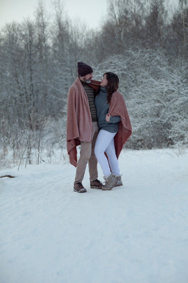 A Couple Standing In The Snow Holding Blankets