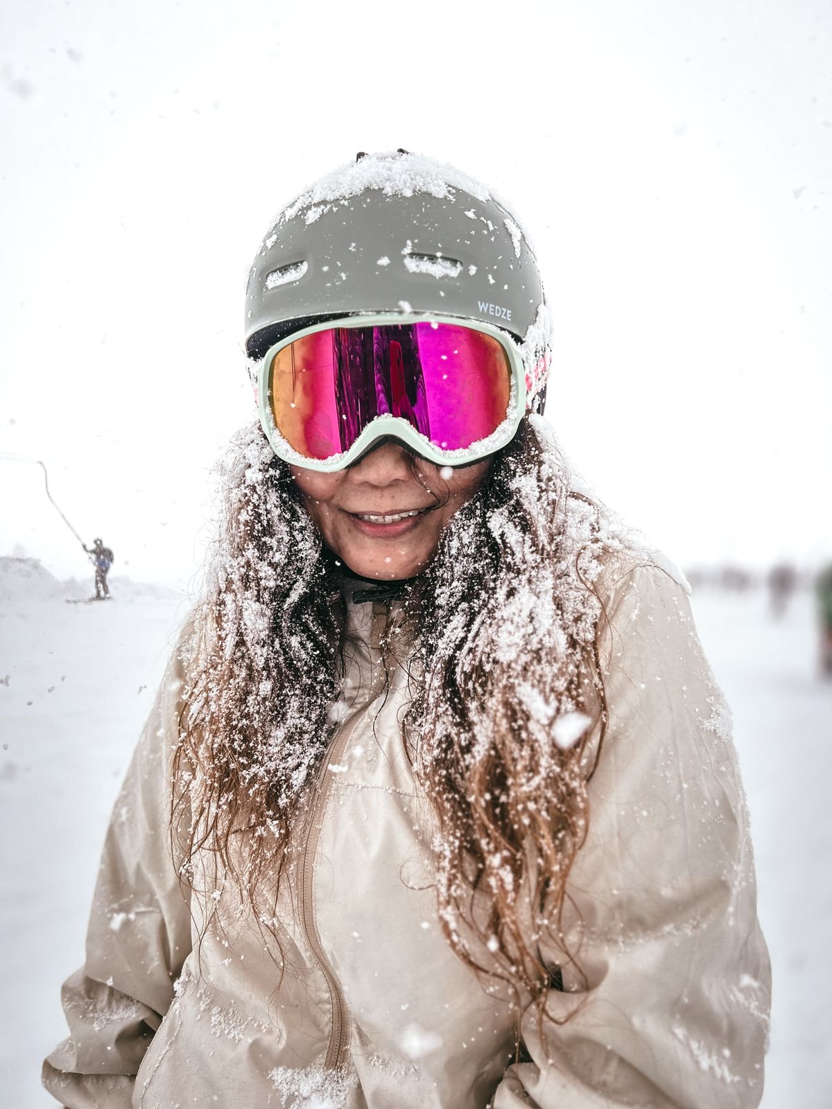 Woman in pink ski goggles and a gray beanie smiling on a snowy slope