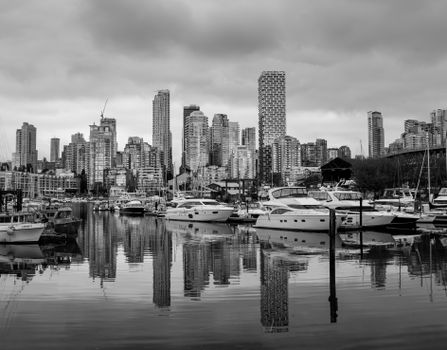 Black and white photo of Vancouver's skyline with yachts in foreground reflecting on water.