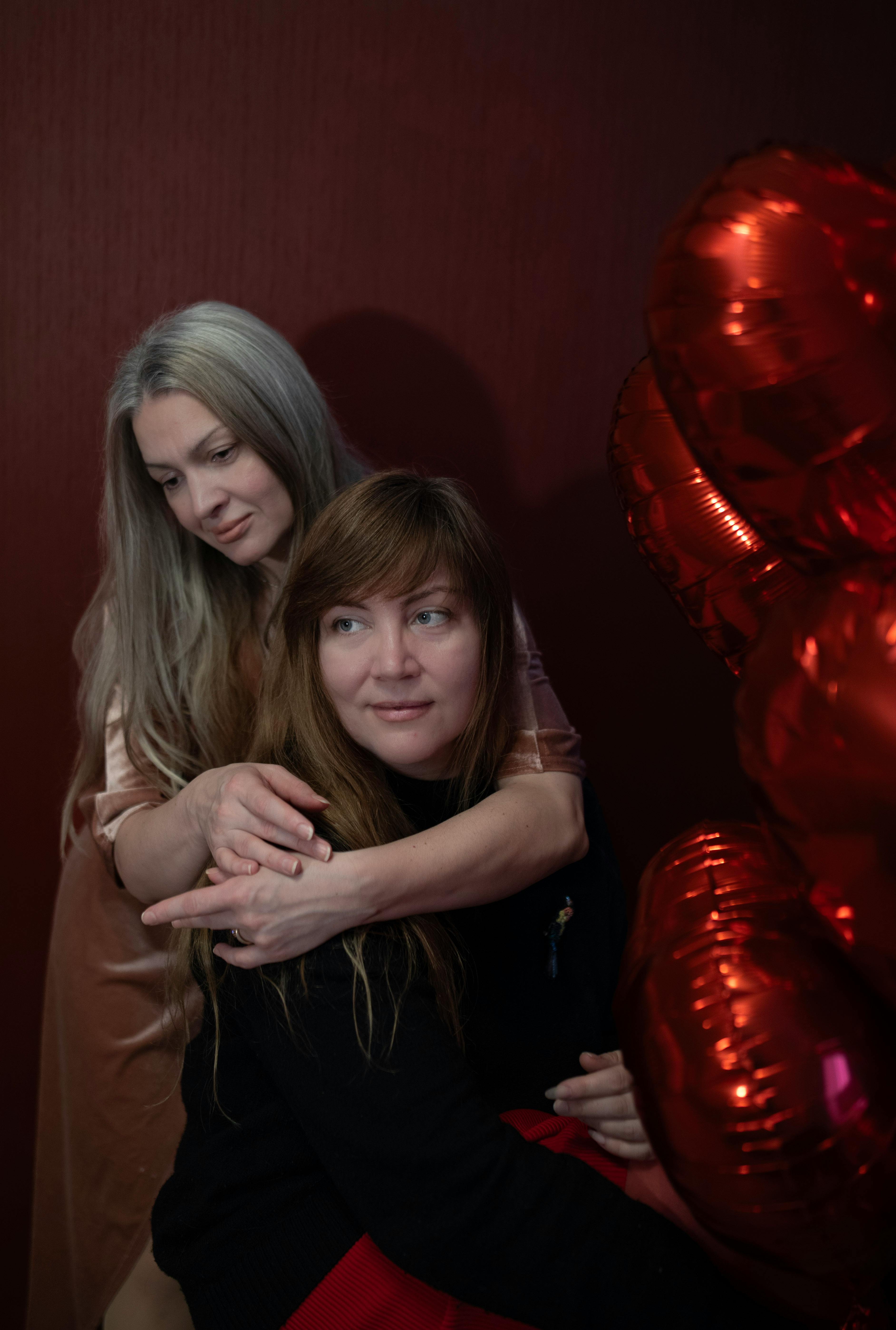 A heartfelt portrait of two women embracing, surrounded by red heart-shaped balloons.