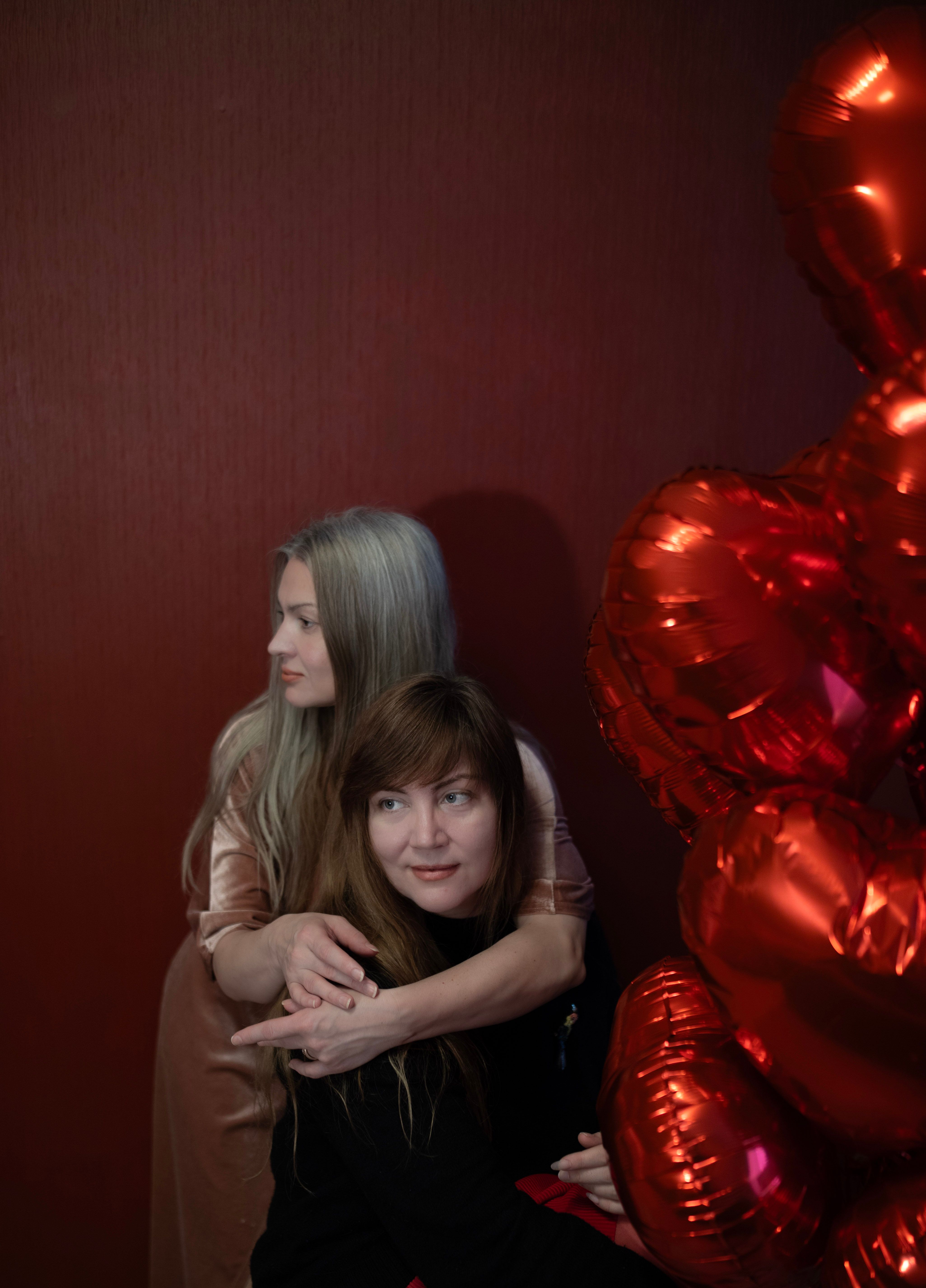 Two women embracing with heart-shaped balloons, conveying love and warmth.
