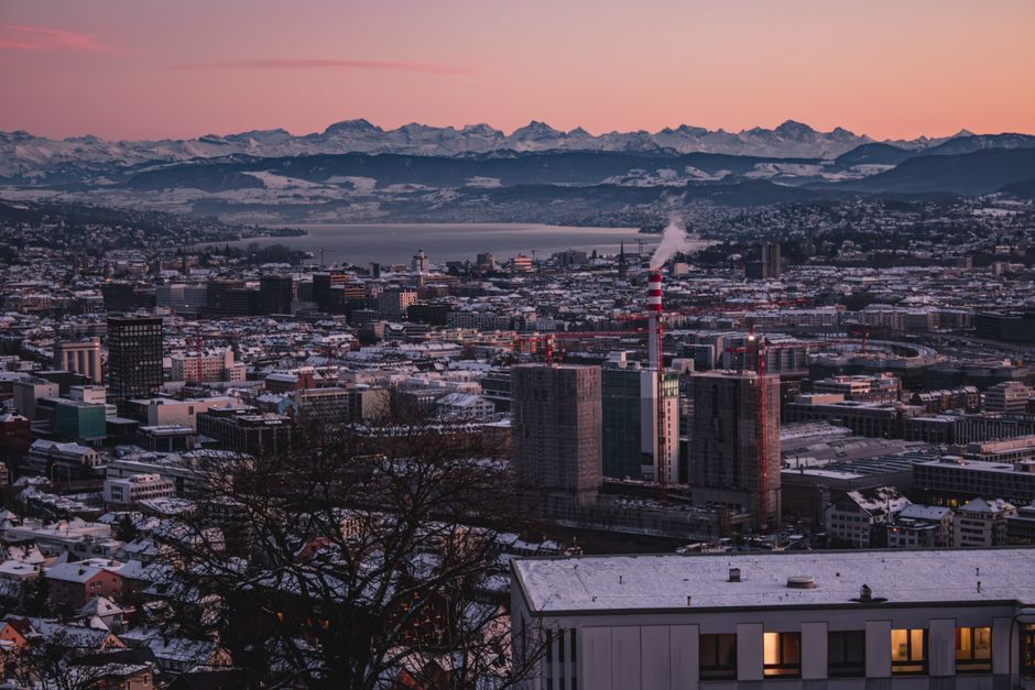 Aerial view of Zürich cityscape at winter sunset with snowy Alps backdrop.