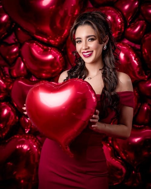 A woman in a red dress holding a large heart shaped balloon