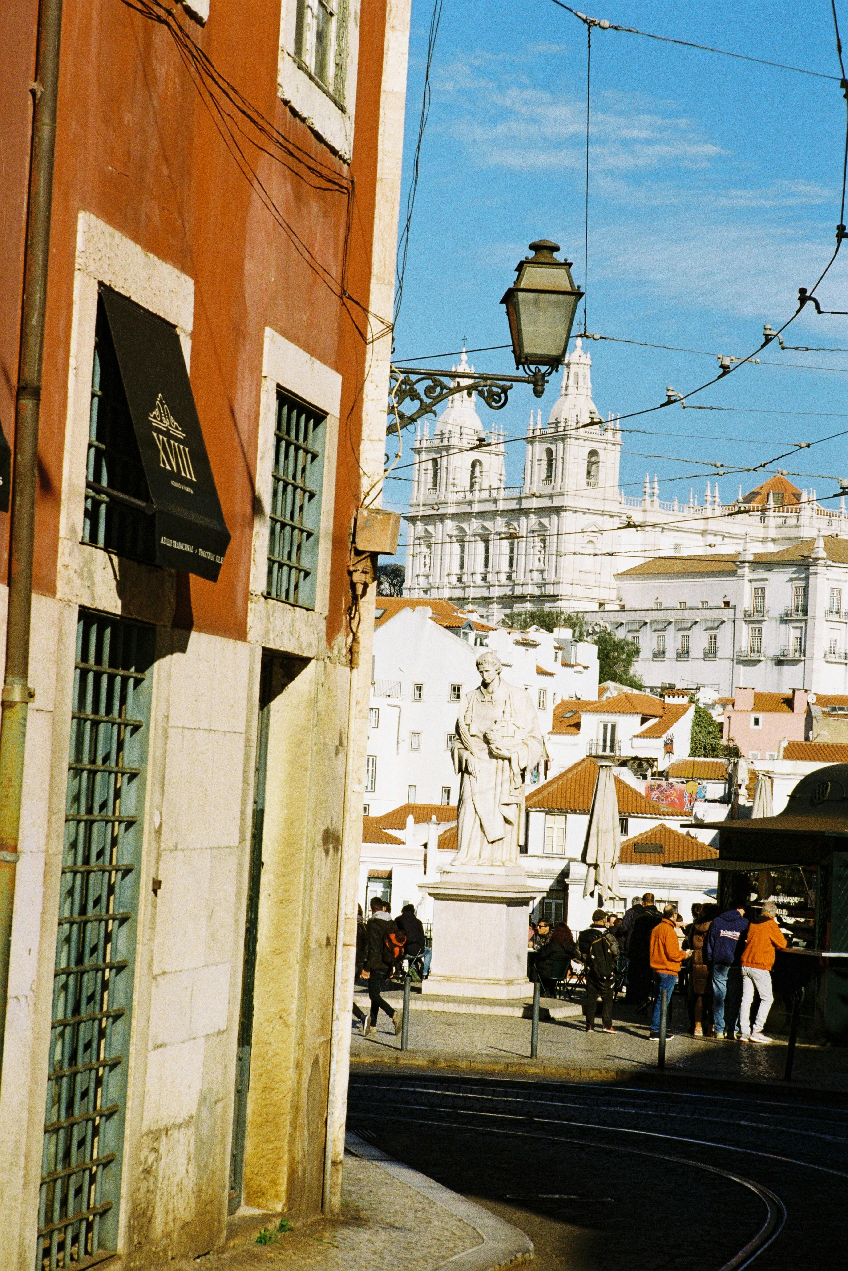 Charming Lisbon street view highlighting Alfama's architecture and a prominent statue under a clear blue sky.