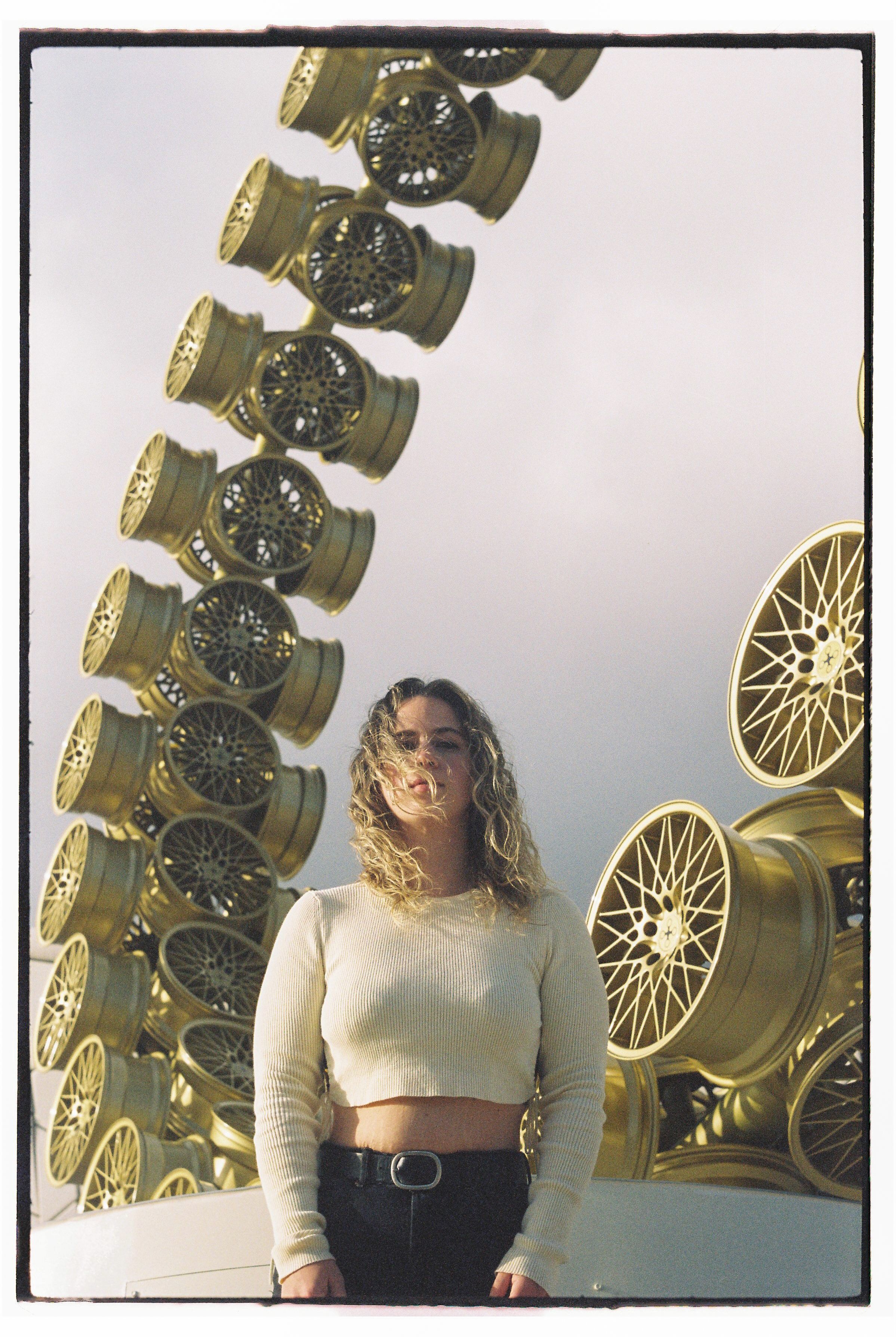 Woman stands before an artistic wheel sculpture in Lisbon, blending fashion and modern art.