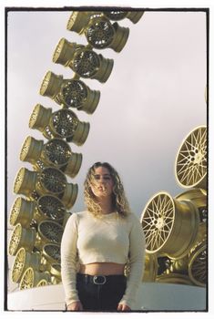 Woman stands before an artistic wheel sculpture in Lisbon, blending fashion and modern art.