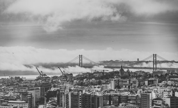 Black and white cityscape of Lisbon featuring the iconic 25 de Abril Bridge amidst rolling clouds.
