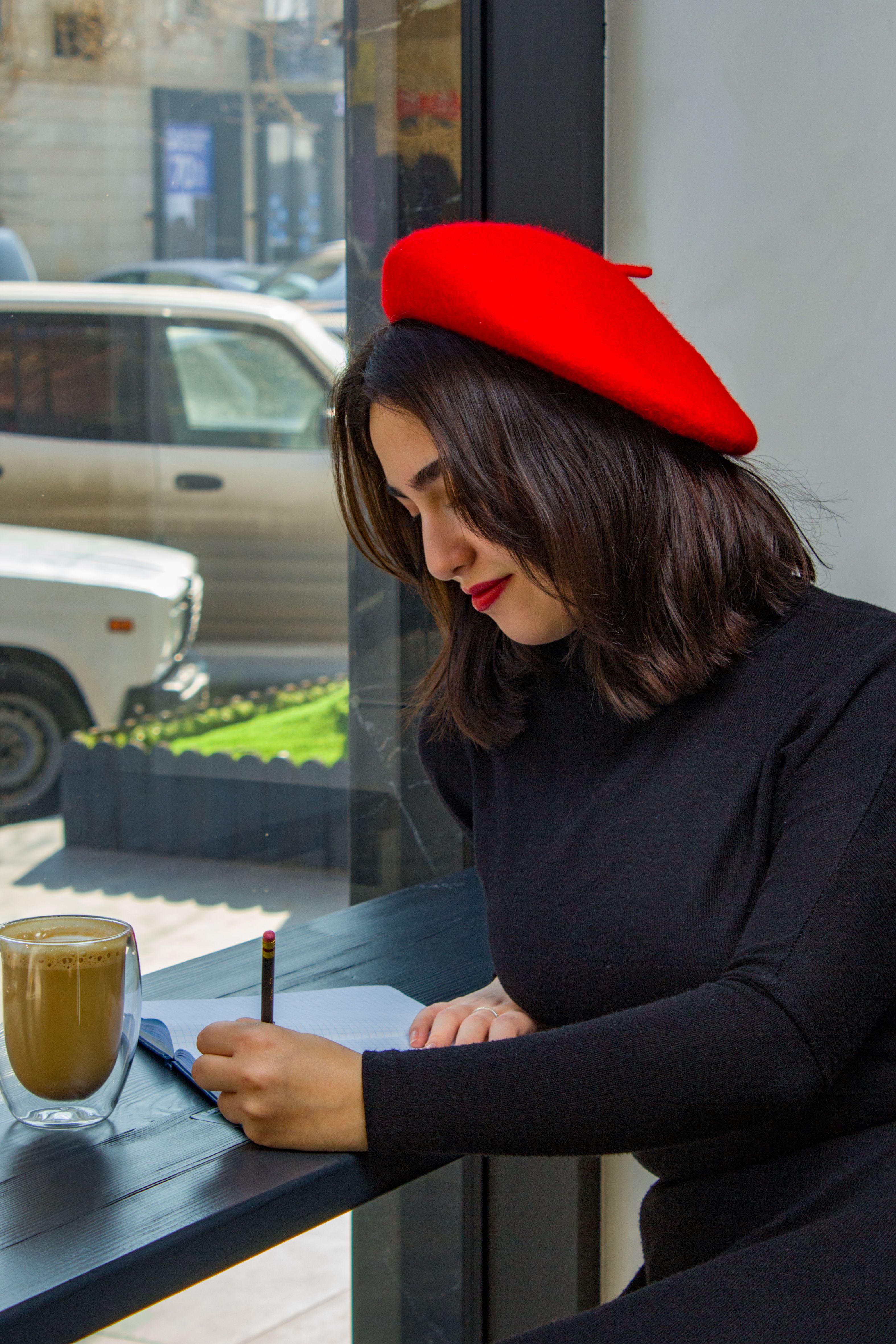 Woman in Red Beret Sitting by Window at Cafe and Writing · Free Stock Photo