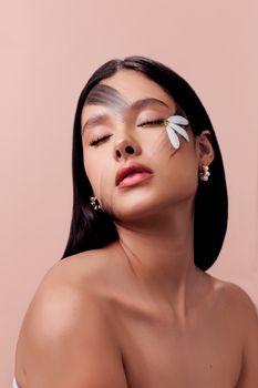A woman posing gracefully with a daisy petal on her cheek against a soft peach background.