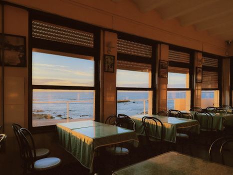 Interior of a seaside restaurant in Porto, Portugal with ocean views through large windows.
