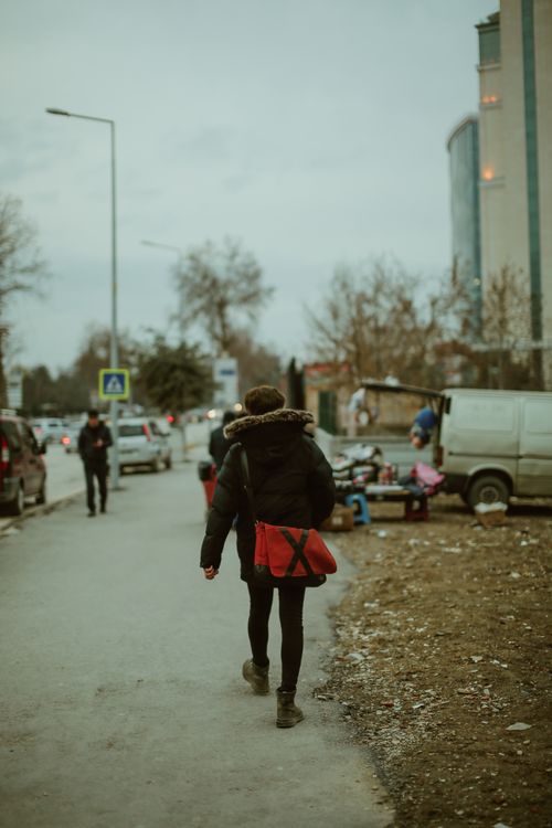 Free A person walks down a city street with buildings and market stalls in the background. Stock Photo