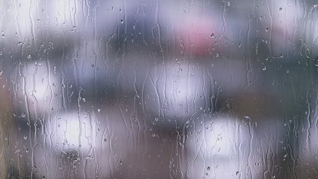 Blurred view of rain on a glass window, creating a moody aesthetic.